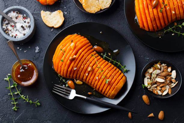 Roasted pumpkin with honey sauce and herbs on a black plate. Slate background. Top view.