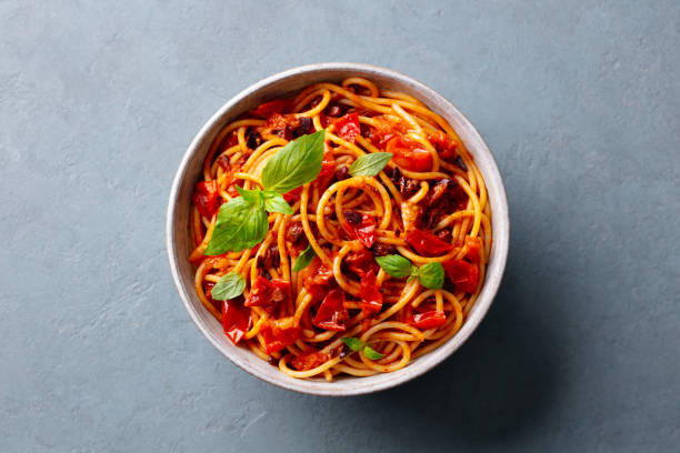 Pasta, spaghetti Puttanesca with tomato sauce and fresh basil. Grey background. Close up. Top view.