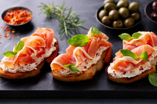istock Bruschetta, crostini with Jamon, ham and fresh basil on dark marble board. Close up. 2174608206