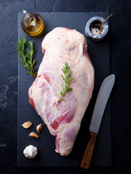 istock Raw lamb leg with spices and herbs on marble cutting board. Dark background. Top view. 2174608452