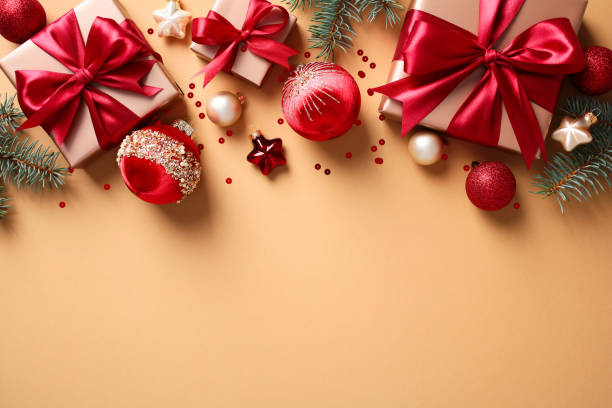 istock Top view festive Christmas decorations on beige background. Flat lay frame border of gift boxes with red ribbon, baubles, pine branches, and stars 2174608489