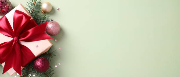 istock Christmas banner with gift box with a red ribbon, pine branches, and sparkling Christmas baubles on a green background 2174608702