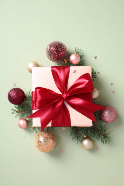 istock Festive gift box with a red bow surrounded by Christmas decorations and fir branches on pastel green background 2174609508