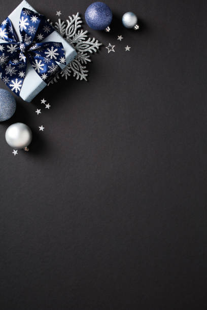 istock Elegant Christmas or winter holiday decor on dark backdrop featuring a blue gift box, silver and blue baubles, snowflake ornaments, and stars 2174611019