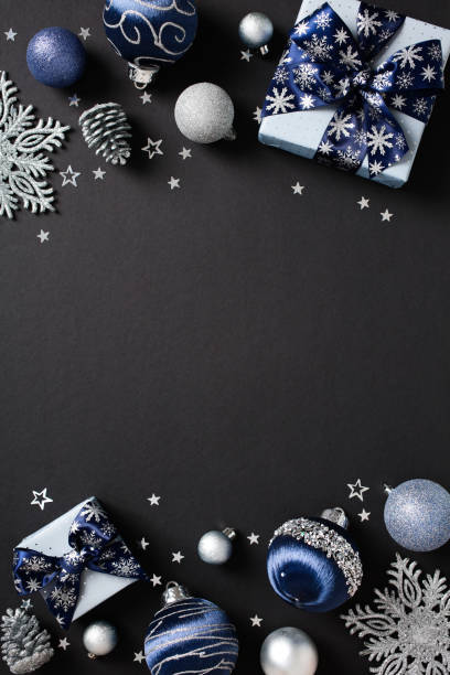 Christmas vertical flat lay composition with gift boxes, snowflake ornaments, confetti, baubles in blue and silver hues on dark background.