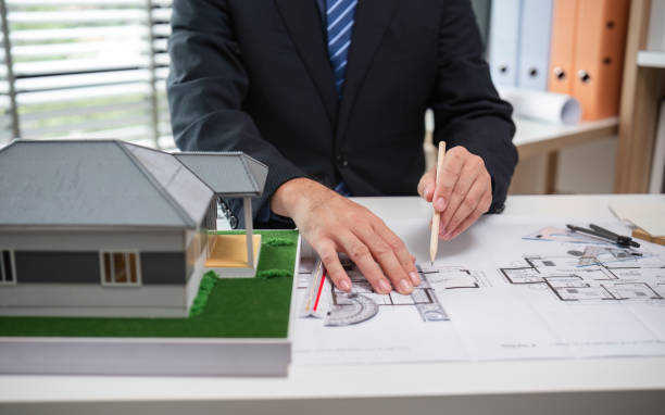 istock Real Estate Project Sales Representative Discussing Architectural Plans with Model House on Desk 2174613991