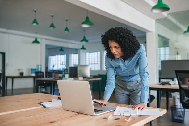 istock Focused young businesswoman standing at her desk using a laptop 2174624433