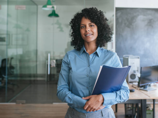 istock Smiling young businesswoman carrying paperwork while standing in an office 2174627103