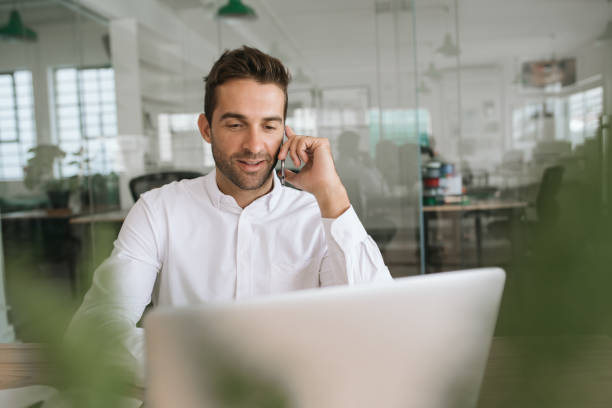 istock Smiling young businessman talking on a cellphone at work 2174639666