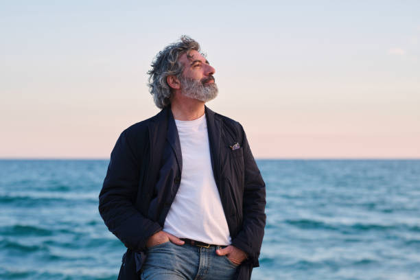 front view portrait of an old caucasian man looking to the side, breathing deeply and smiling while enjoying the sea breeze in a tranquil setting on a winter day. stock photo