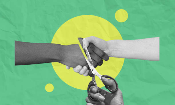 Two hands locked in a handshake cut by a pair of scissors