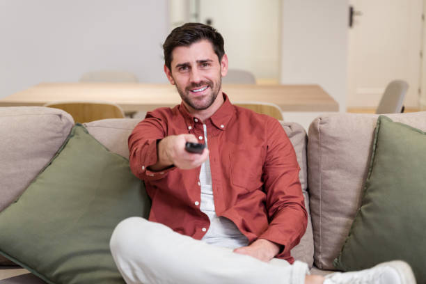 istock Happy man watching tv changing channels sitting on sofa at home 2174660062