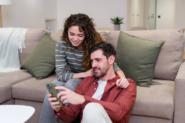 istock Young couple relaxing on sofa at home browsing internet on smartphone 2174660082
