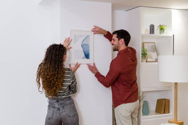 istock Young couple hanging a picture frame on a white wall 2174660125