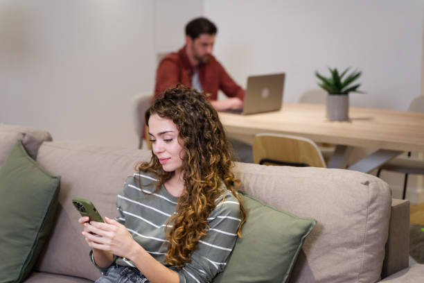 istock Young woman using smartphone while man working on laptop in background 2174660206