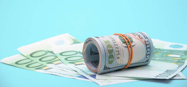 istock Roll of dollars surrounded by hundred euros bills 2174661461