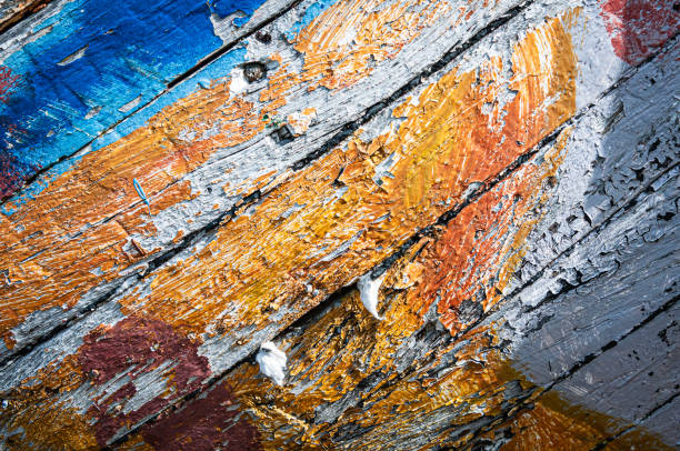 Peeling, cracked paint of blue and orange colors and white cotton caulking on the hull of an old wooden boat on the dock in Nuuk, Greenland