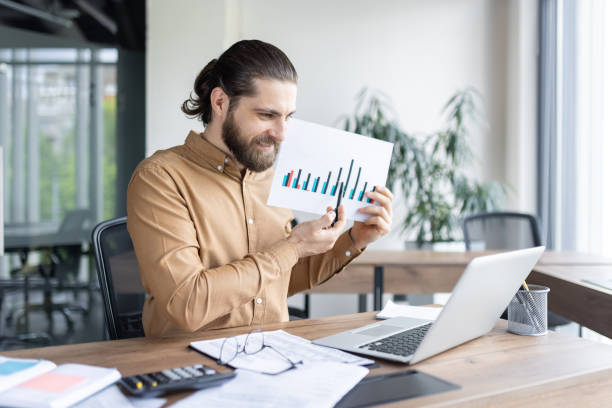 istock Confident businessman presenting financial data in modern office with laptop and charts. 2174662518
