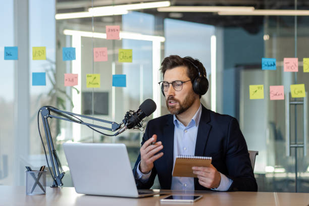 istock Business professional conducting podcast in modern office setting using microphone and laptop for online communication 2174665864