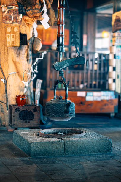 A traditional Japanese iron kettle hanging over a fireplace in a rustic interior setting