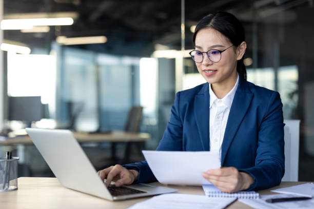 istock Confident Asian businesswoman reviewing documents while working on laptop in modern office environment 2174668630