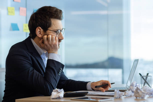 istock Businessman appearing bored with accounting work at office desk with computer and crumpled paper 2174668746