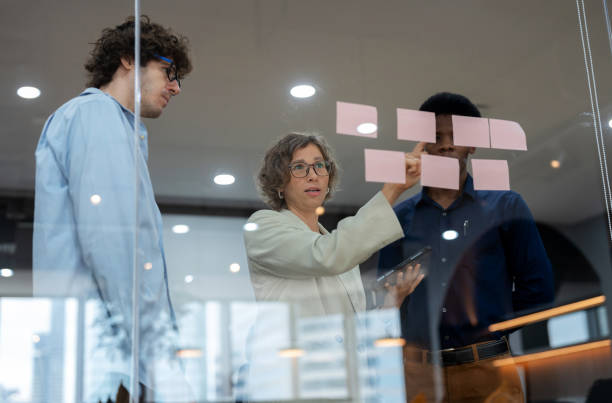 istock A diverse business development team in a start-up office collaborates in a meeting room, discussing new products and service strategies. With post-it notes on the glass windows, the team engages in decision-making and planning to enhance business. 2174670323