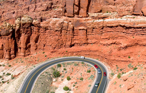 A customized orange Tesla Cybertruck drives along a winding desert highway, surrounded by stunning rock formations and a clear blue sky. The futuristic electric pickup stands out against the rugged landscape, embodying innovation, adventure, and sustainability. Capturing the essence of off-road exploration and modern automotive design, this image is perfect for technology, travel, and automotive enthusiasts.