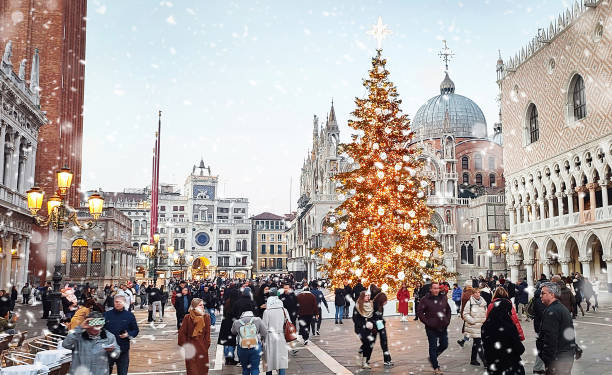Venice, Italy - 25 December, 2023: People enjoying and walking in San Marco square in snowing Christmas evening in Venice. Christmas tree with decorations near Doge's Palace. Italy, Europa.