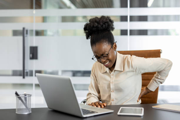 istock Young african american woman experiencing back pain while working at desk in modern office environment 2174671302