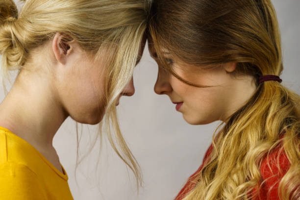 Two cheerful young women hugging each other, looking at camera and smiling