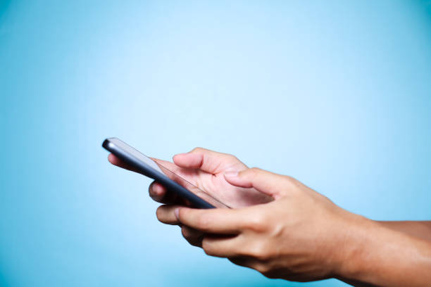 istock Closeup of hand holding or using smartphone on blue background. 2174678279