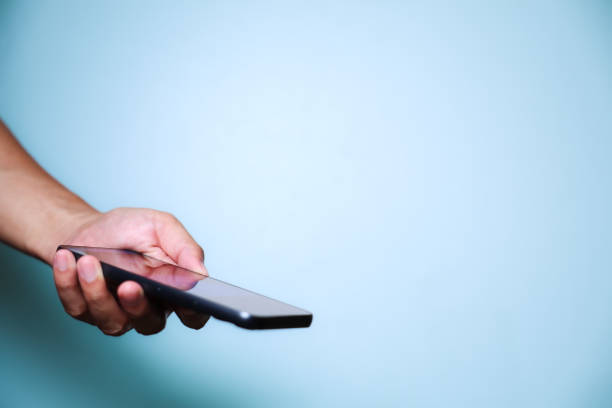 istock Closeup of hand holding or using smartphone on blue background. 2174678314