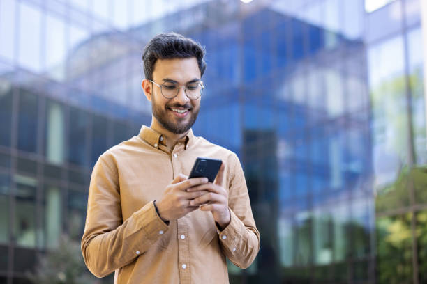 istock Smiling young man using smartphone outside modern office building reflecting urban lifestyle and connectivity 2174678877