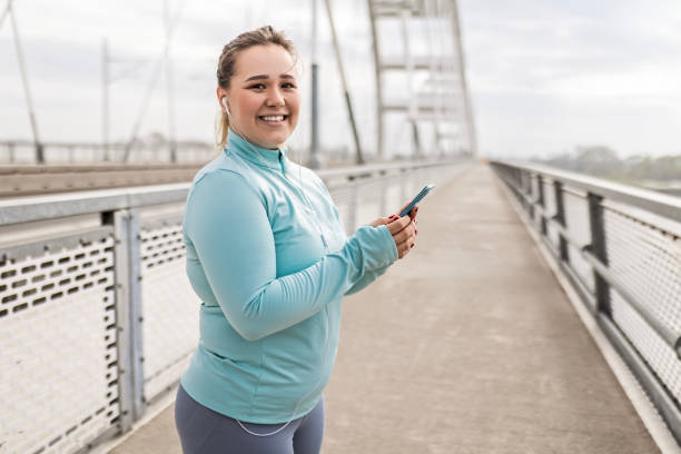 istock Overweight Young Woman Taking a Break During Bridge Workout Using Phone 2174681344