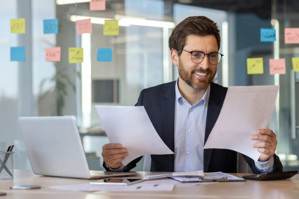istock Confident businessman analyzing documents at his modern office desk surrounded by colorful notes, showcasing productivity and efficiency in the workplace 2174681571