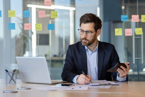 istock Serious financier focused on work with laptop and phone in modern office setting, analyzing data and making critical decisions 2174684880