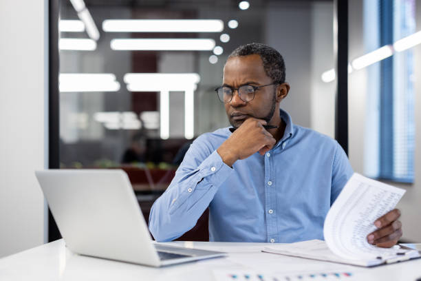 istock Serious businessman deeply engaged in financial analysis while reviewing paperwork at a desk in modern office 2174684927
