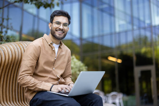 istock Smiling young man working on laptop outside modern building, enjoying remote work on sunny day 2174685104