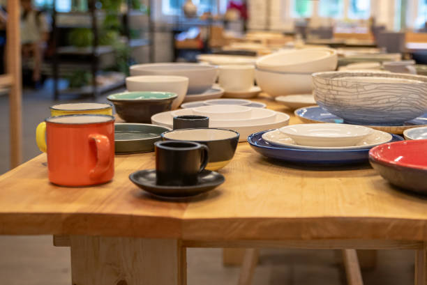 istock Assorted ceramic cups and bowls are displayed on a wooden table in a cozy shop setting, with a blurred background of shelves and plants. 2174686241