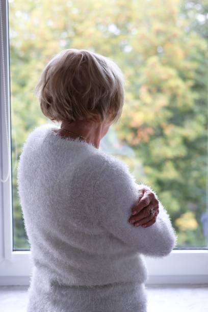istock A lonely elderly woman standing at the window and waiting 2174687934