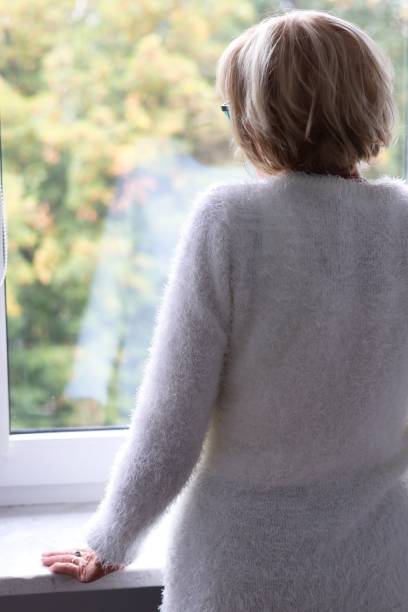 istock A lonely elderly woman standing at the window and waiting 2174687945