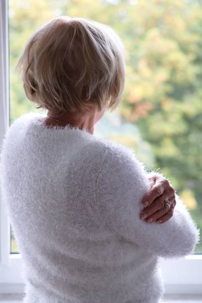 istock A lonely elderly woman standing at the window and waiting 2174687953