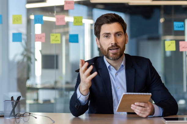 istock Professional businessman engaging in a video call while holding a notebook in a modern office setting, emphasizing business communication and professional interaction 2174689224