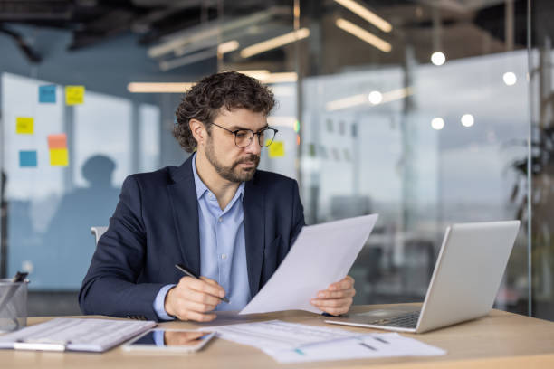 istock Serious businessman analyzing documents at office desk with laptop and papers 2174689535