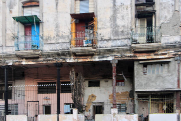 This image showcases a weathered, old building with a lot of character. The structure has peeling paint, exposed brick, and signs of wear and tear, indicating its age and the passage of time. Despite its dilapidated state, the building’s balconies stand out with splashes of color. The doors on the balconies, one blue and one red, add vibrancy to the scene. The worn-out facade tells a story of history and resilience, while the colorful accents hint at the life still present within. The overall mood evokes nostalgia and urban decay.