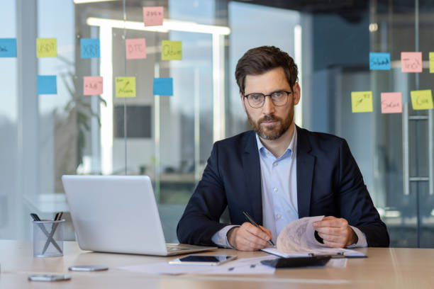 istock Serious thinking mature businessman working at desk with laptop and documents in modern office setting 2174691278