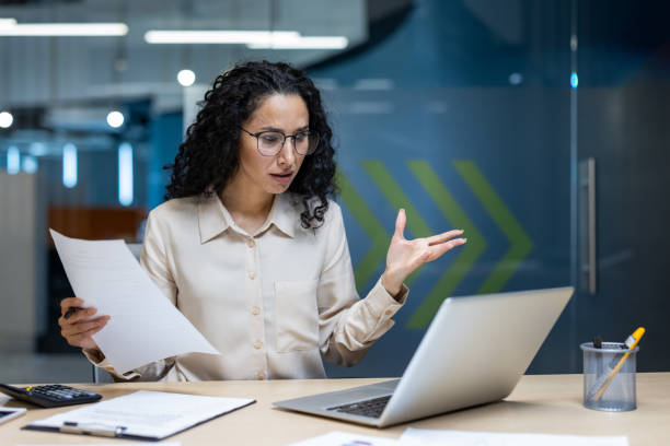 istock Stressed businesswoman with documents and laptop expressing frustration during office work in modern corporate environment. 2174692295