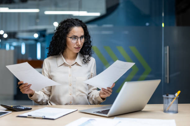 istock Hispanic businesswoman intently reviewing documents at desk in modern office setting with serious expression 2174696553