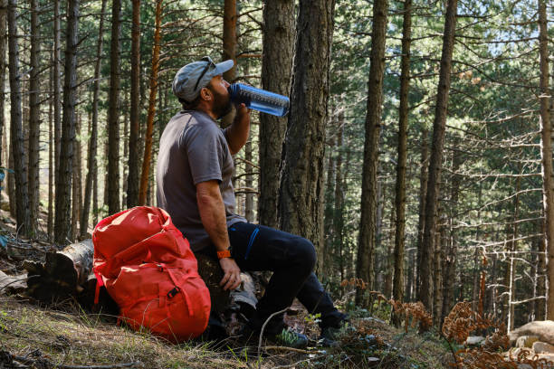 istock Male hiker sitting on logs resting while drinking water. 2174699951